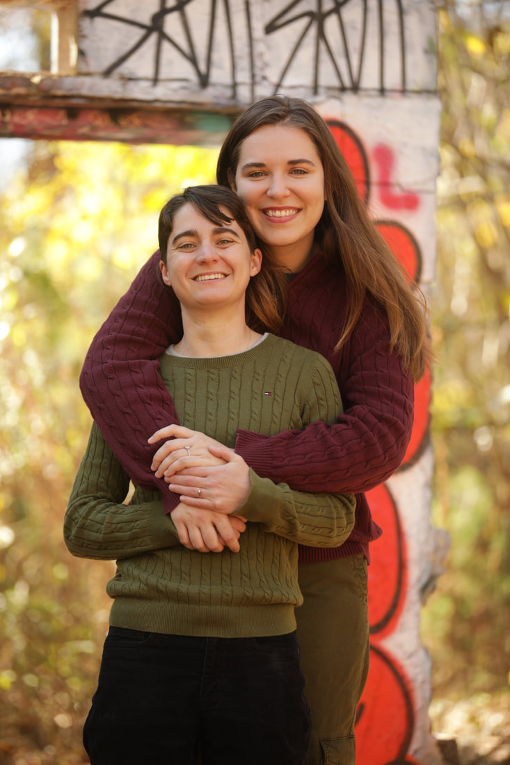 A women with short brown hair, wearing a green sweater is being hugged by a tall blonde women with long hair wearing a maroon sweater.
